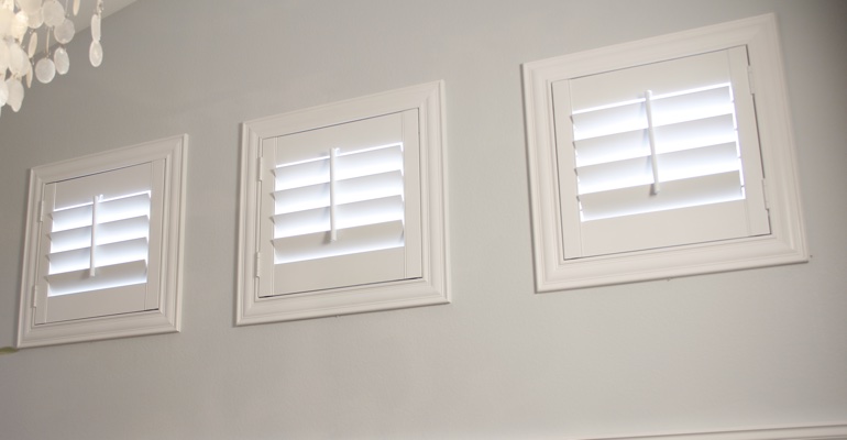 White shutters on three small square windows in laundry room